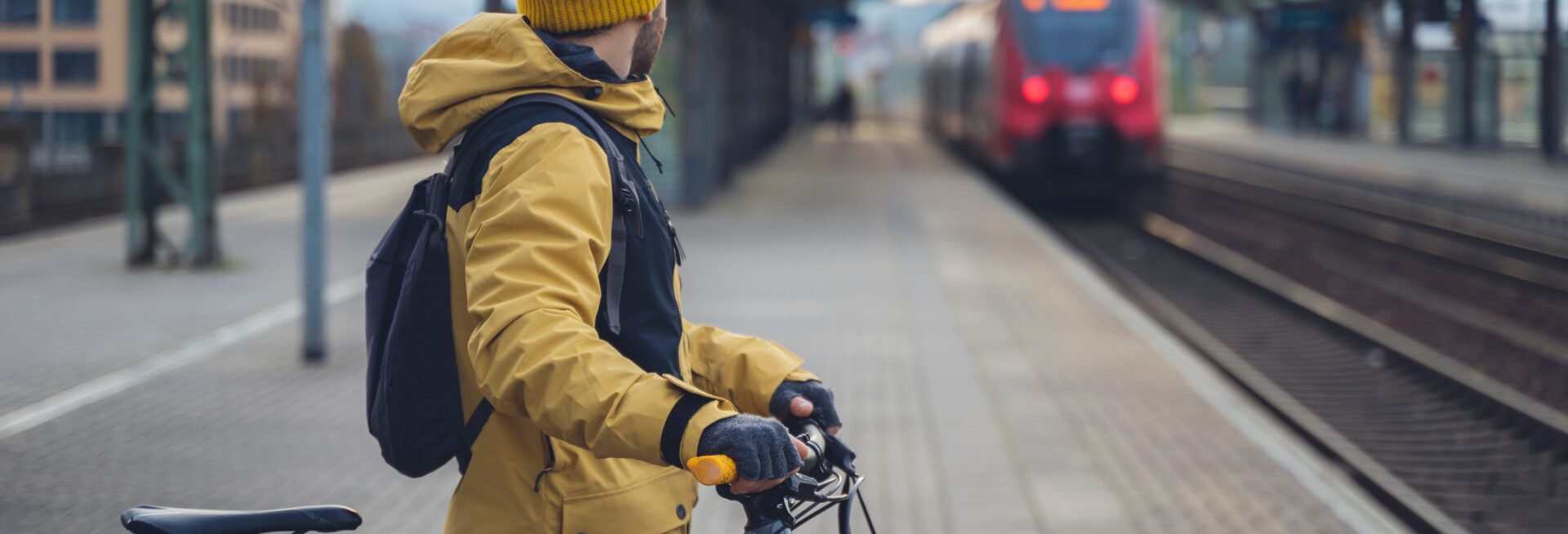 A man in winter clothes, waiting with his bike, the train. In the background the train that is about to arrive.