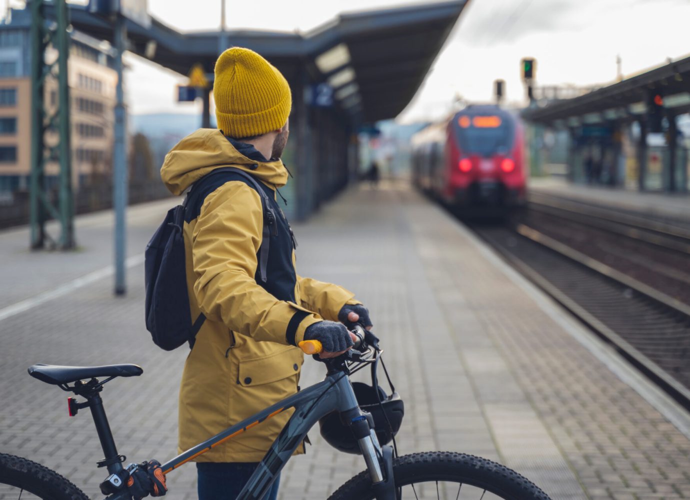 A man in winter clothes, waiting with his bike, the train. In the background the train that is about to arrive.